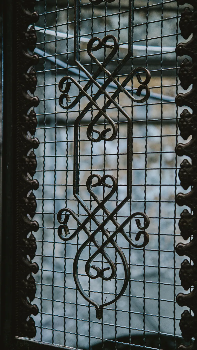 Gros plan macro sur une grille en fer forgé noir, motif ouvragé symétrique en volutes