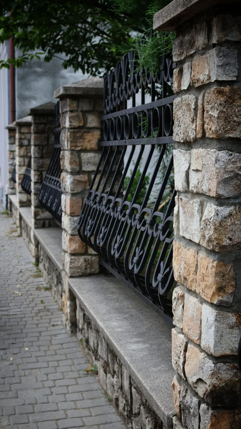 Clôture en fer forgé noir à motif ondulé entre deux piliers en pierre naturelle