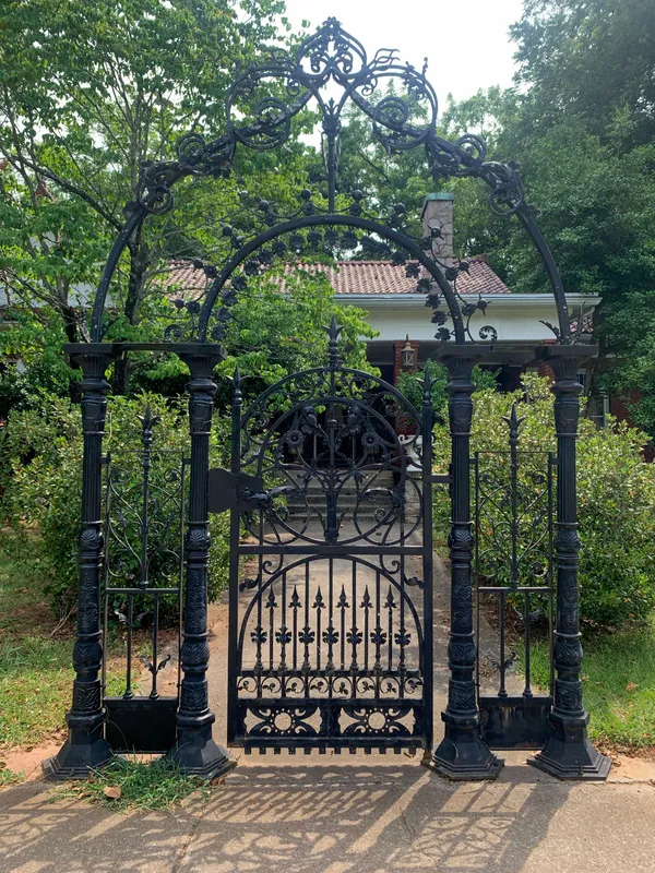 Portail-arche en fer forgé noir très ouvragé, volutes et pointes de lance, à l'entrée d'un jardin arboré